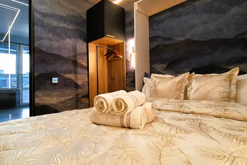 Изолированная спальня с аккуратно заправленной двуспальной кроватью с ортопедическим матрасом. Комплект чистых пушистых полотенец для гостей.